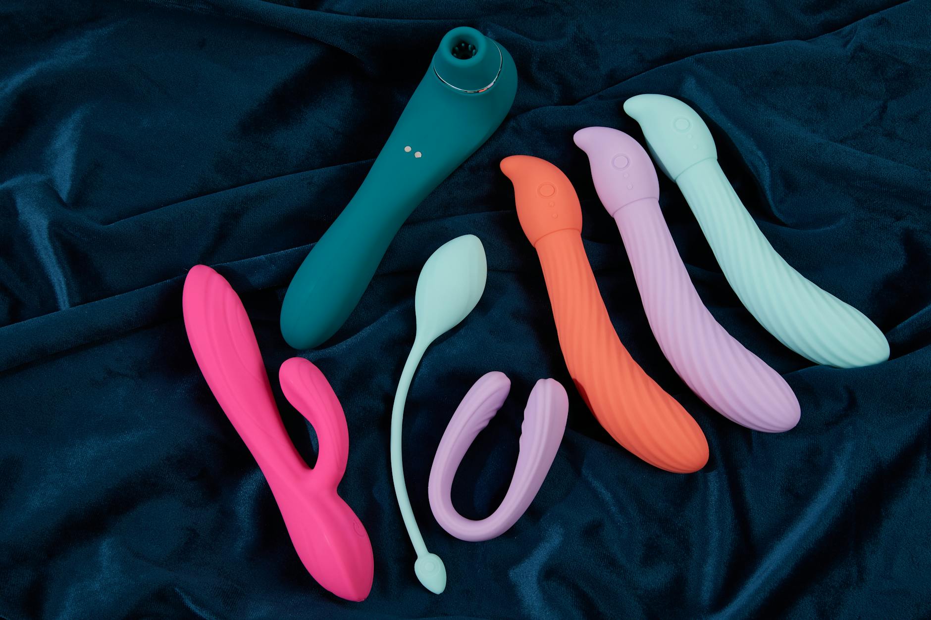 Un arrangement minimaliste de jouets sexuels colorés sur un tissu bleu foncé, montrant la diversité des options de plaisir