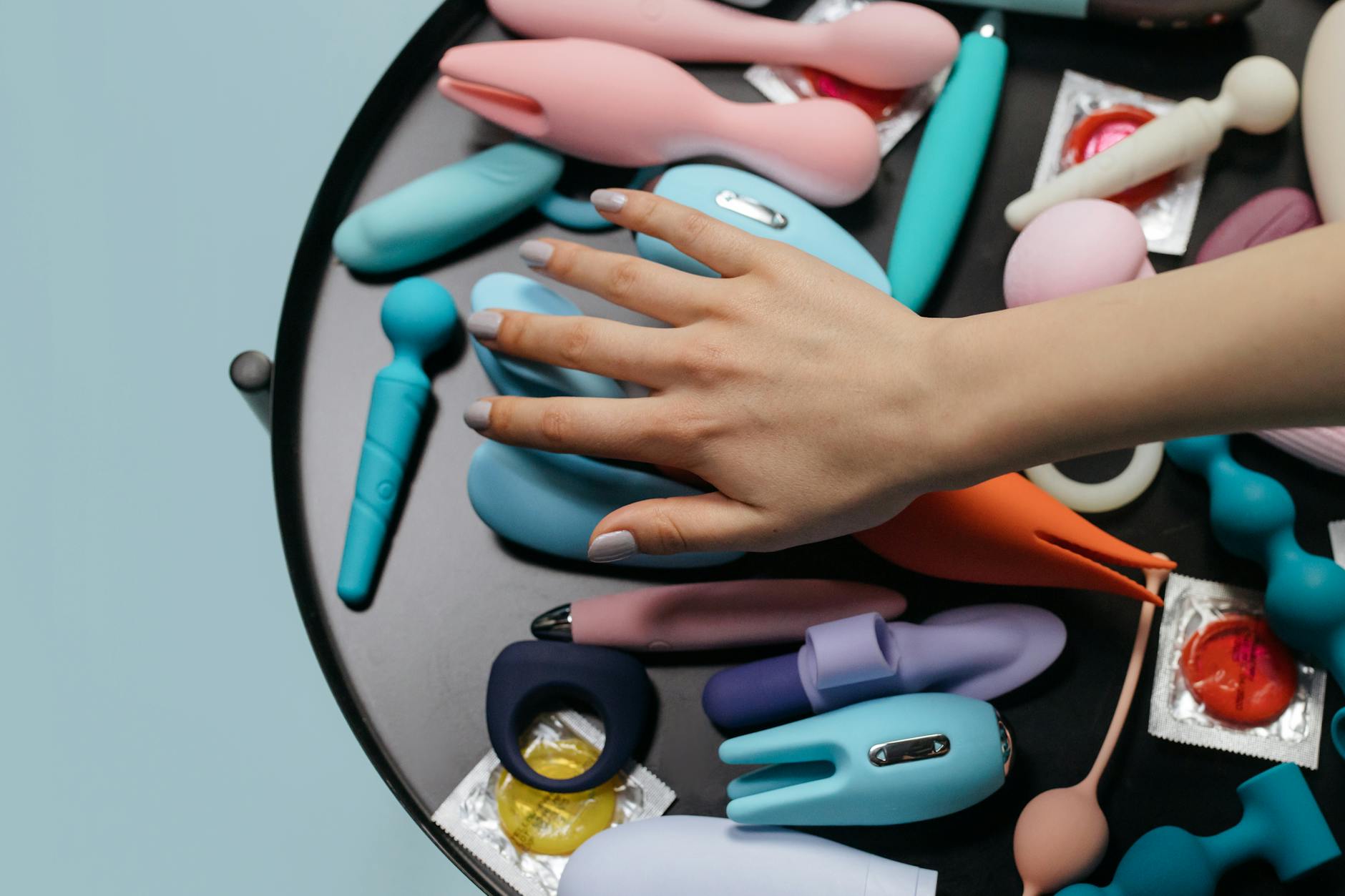Une main tendant un vibromasseur citron parmi une sélection de jouets sexuels colorés sur une table