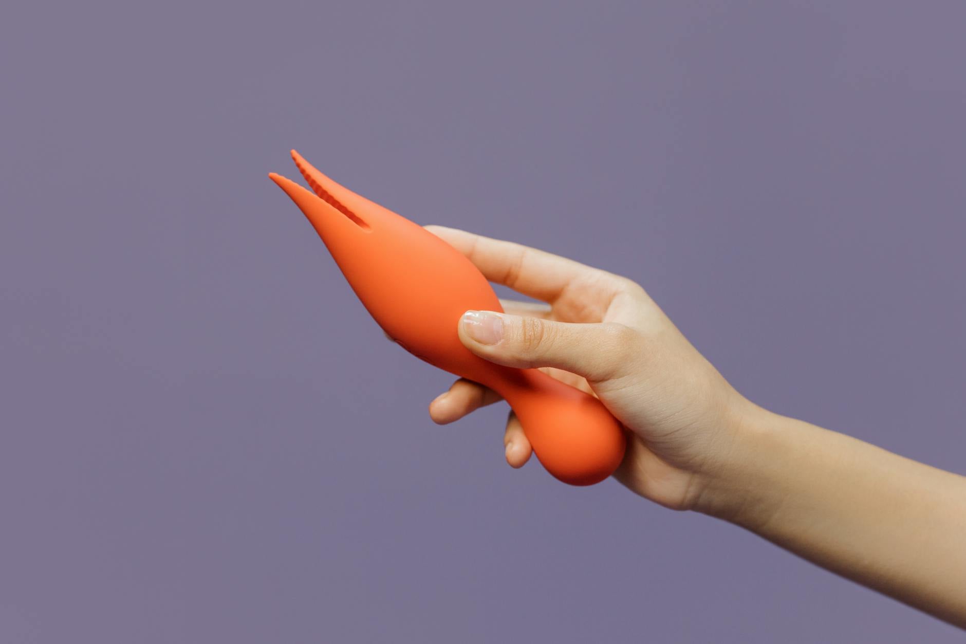 Une main tenant un vibromasseur orange vif sur un fond violet minimaliste, symbolisant la sensualité moderne.