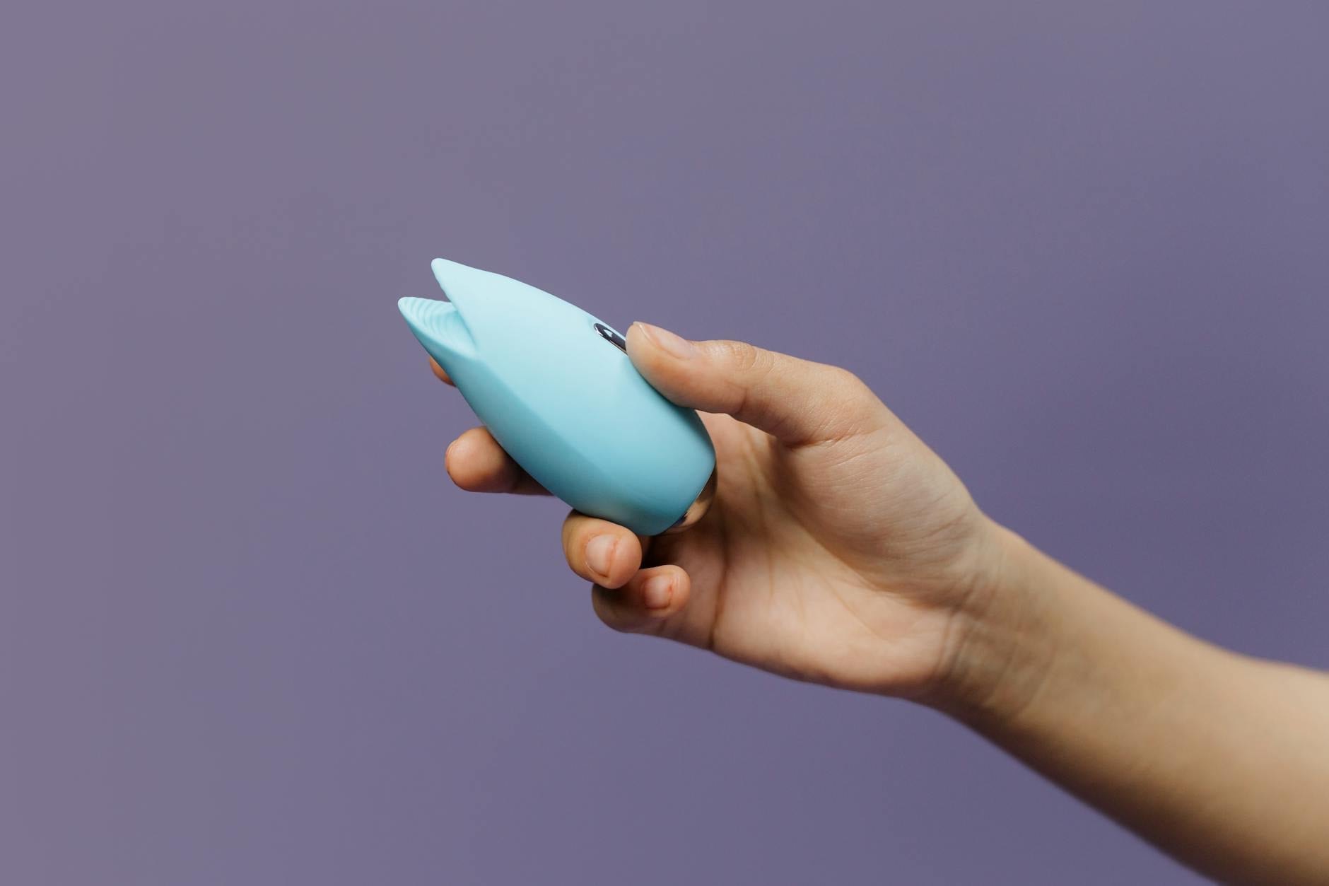 Deux mains tenant des vibromasseurs colorés contre un fond pastel rose et bleu