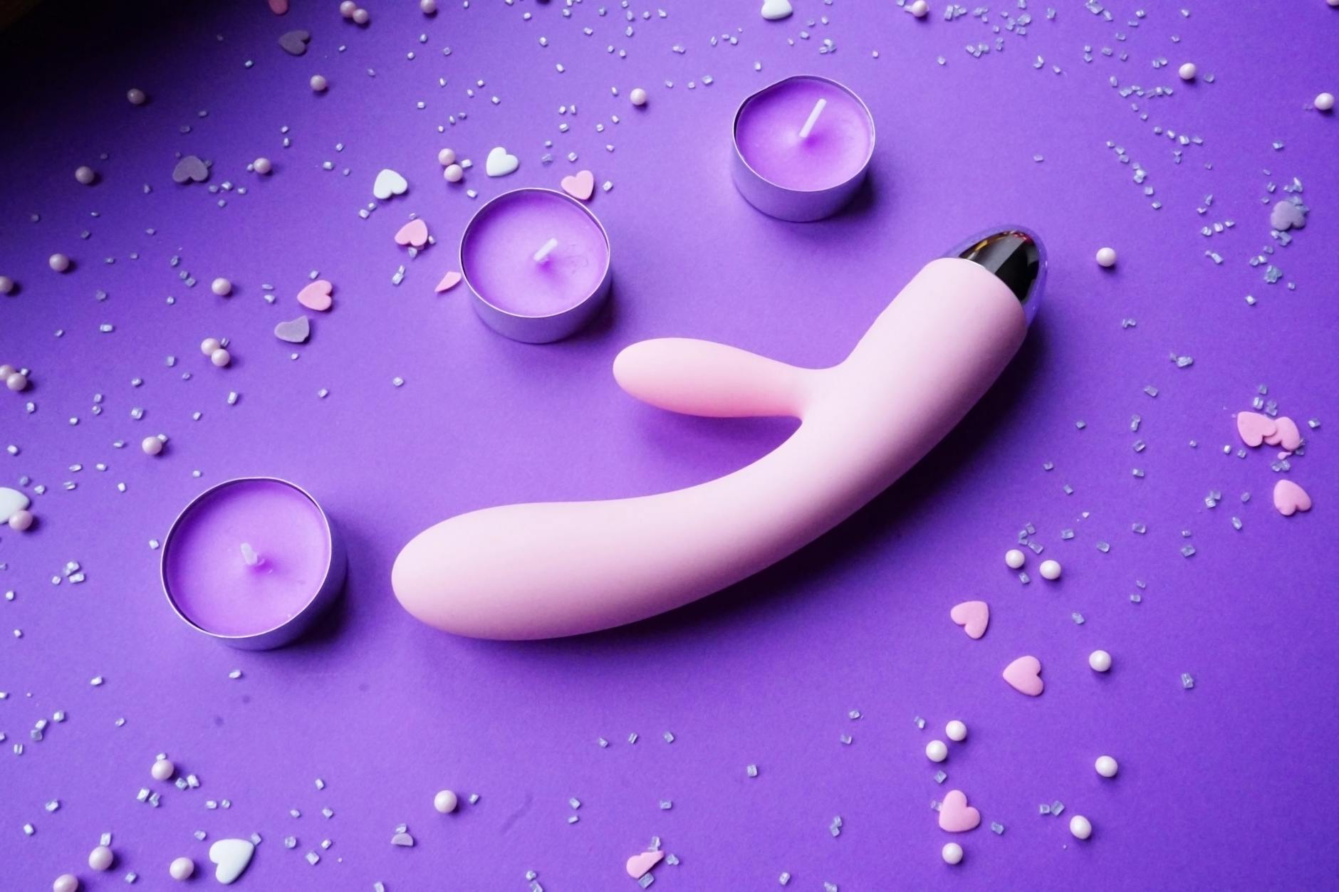 Un vibrateur rose vif sur un fond violet avec des confettis en forme de cœur, créant une ambiance romantique.